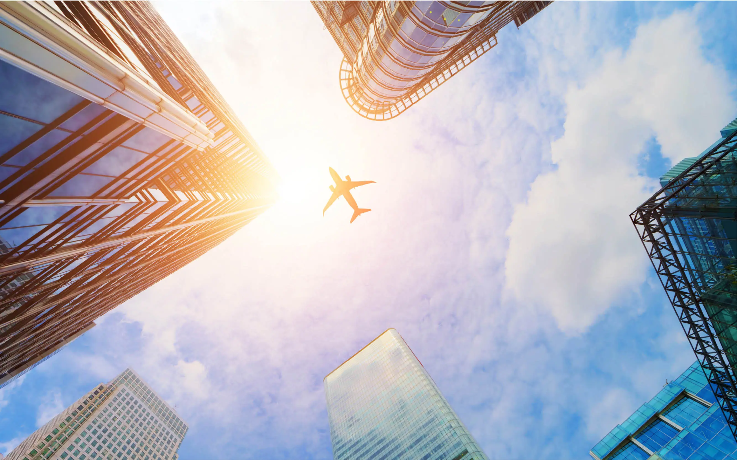 plane flying with bright sun and buildings in background